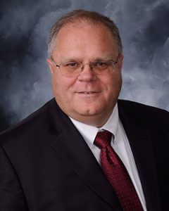A man smiling in a black suit and dark red tie