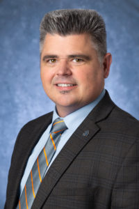 A man smiling wearing a grey suit