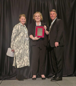 Jessica Carter, Rachel Prather and Ted Rogalski stand on a stage for a photo