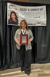 Lindsey Culver holds her plaque in front of a banner
