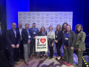 A group of rural health care professionals stand together holding a sign that reads "I Love Rural Health"